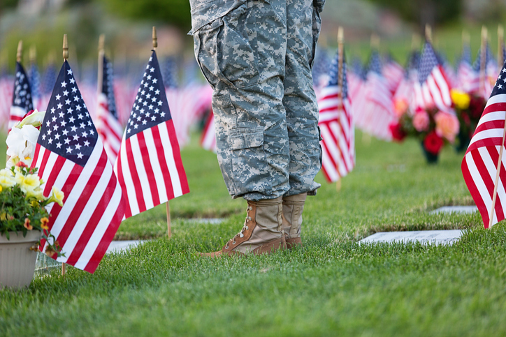 A soldier stands among graves marked with American Flags on Memorial Day